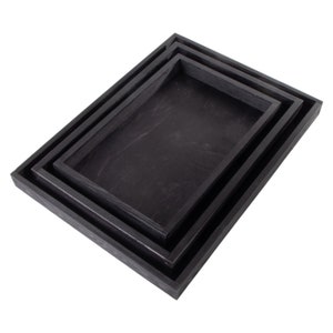 May include: Three black wooden trays of varying sizes, nested together. The trays are made of a dark wood with a smooth finish.