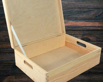 May include: A natural wood box with a hinged lid and a white ribbon closure. The box has two handles on the sides and is open to reveal the empty interior.