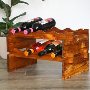 May include: A wooden wine rack with two shelves, holding six bottles of wine. The rack is stained a dark brown color and has a rustic appearance.