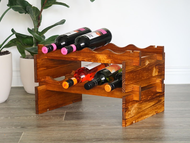 May include: A wooden wine rack with two shelves, holding six bottles of wine. The rack is stained a dark brown color and has a rustic appearance.