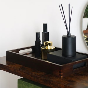 Puede incluir: Una bandeja de madera marrón oscuro con botellas negras y doradas y un difusor negro con palitos sobre una mesa de madera marrón oscuro.