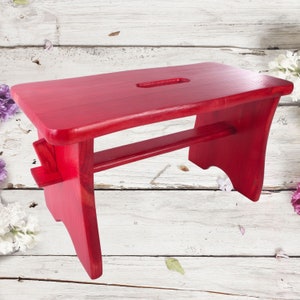 May include: A solid red wooden step stool with a rounded top and a cutout handle. The stool has a simple design and is perfect for reaching high places.