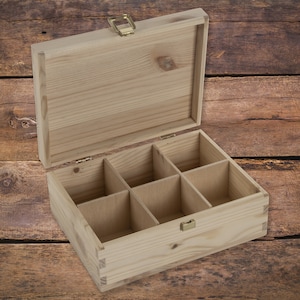 May include: A wooden box with a hinged lid and six compartments. The box is made of light-colored wood and has a brass latch.