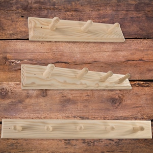 Könnte beinhalten: Drei Wand-Kleiderhaken aus Holz mit unterschiedlichen Längen und Anzahlen an Haken. Die Haken sind aus Naturholz gefertigt und haben einen rustikalen Look.