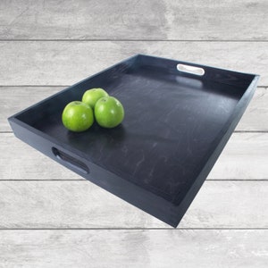 May include: A black wooden serving tray with rounded edges and two handles on the sides. The tray is filled with three green apples.