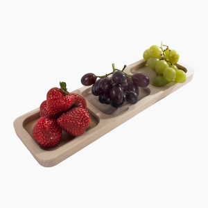 Könnte beinhalten: Ein Holztablett mit drei unterteilten Abschnitten, die jeweils mit einer anderen Sorte Obst gefüllt sind: rote Erdbeeren, dunkelviolette Trauben und grüne Trauben.