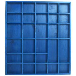 Op de afbeelding: Blauw houten displayrek met meerdere compartimenten. Het rek is geschilderd in een effen blauwe kleur, waarbij de houtnerf zichtbaar is. De compartimenten zijn in een rasterpatroon gerangschikt. Ideaal voor het presenteren van kleine items.