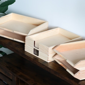 Peut inclure: Ensemble d'organisateurs de bureau en bois non fini. L'ensemble comprend des plateaux à lettres et un porte-documents, tous fabriqués en bois de couleur claire. Les organisateurs sont disposés sur une surface en bois foncé, mettant en valeur leur grain naturel et leur design simple.