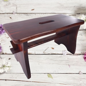May include: A dark brown wooden step stool with a cutout handle on the top. The stool is made of solid wood and has a rustic look.