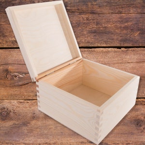 May include: An empty wooden box with the lid open. The box is made of light-coloured wood and has a simple design.