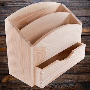 Puede incluir: Un organizador de escritorio de madera clara con tres ranuras curvas y un cajón extraíble. El organizador está hecho de madera sin terminar, mostrando la veta natural. El diseño es simple y funcional, adecuado para la oficina o el hogar.