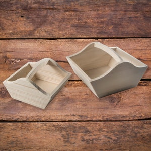 Può includere: Due cesti di legno, uno più grande dell'altro, sono mostrati su una superficie di legno. Entrambi i cesti hanno un manico e sono fatti di legno naturale.