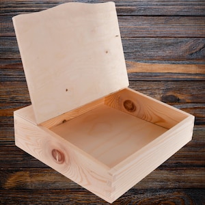 May include: An empty wooden box with a hinged lid. The box is made of light-colored wood and has a natural finish. The lid is open and the inside of the box is visible.
