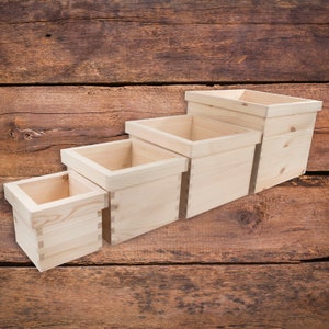 May include: Four wooden boxes of varying sizes, stacked on top of each other, with the largest box at the top and the smallest box at the bottom. The boxes are made of natural, light-coloured wood and have a smooth, unfinished surface.