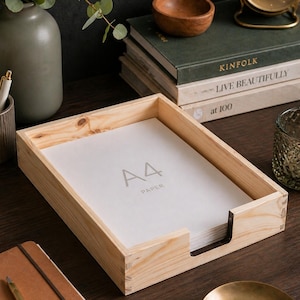 May include: A light-colored wooden desk tray filled with A4 paper. The tray is rectangular with a cutout on one side for easy access. The text "A4 PAPER" is printed on the paper. Other desk accessories are in the background.