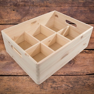 Può includere: Una cassa di legno con sei scomparti, perfetta per organizzare e riporre piccoli oggetti. La cassa è realizzata in legno naturale e ha un aspetto rustico.