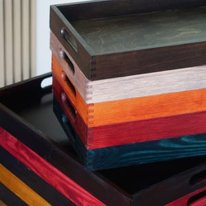 May include: A stack of five wooden trays in various colors, including black, red, orange, gray, and teal. The trays are all rectangular and have a smooth finish.