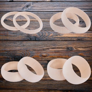 May include: Six wooden bangles in various sizes and arrangements. The bangles are light brown and have a smooth, polished finish.