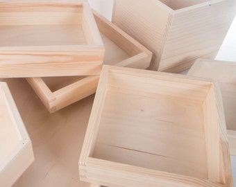 May include: A collection of light-colored, unfinished wooden boxes and trays of varying depths and sizes. The items feature visible wood grain patterns and interlocking corner joints, showcasing a natural, pale beige tone throughout the set.