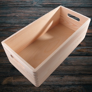 Puede incluir: Una caja de almacenamiento de madera natural con forma rectangular y un asa en la parte superior. La caja está vacía y tiene un acabado de madera clara.