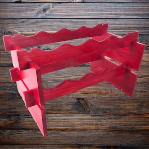 May include: A red wooden wine rack with three tiers. The rack is made of unfinished wood and has a rustic look.