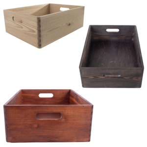 Puede incluir: Tres cajas de almacenamiento de madera con asas. Las cajas están hechas de madera natural y están teñidas en diferentes colores: natural, marrón oscuro y marrón rojizo.