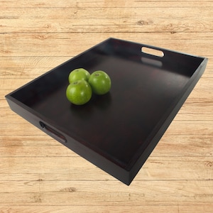 May include: A dark brown wooden serving tray with two handles on the sides. The tray is empty except for four green apples.