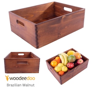 Puede incluir: Una caja de madera de nogal brasileño con dos asas a cada lado. La caja está vacía en la primera imagen y llena de fruta en la segunda imagen.