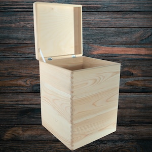 Puede incluir: Una caja de madera de color claro con una tapa con bisagras, abierta para revelar el interior. La caja está construida con juntas de cola de milano y tiene un acabado de veta de madera natural. El fondo es una superficie de madera oscura.