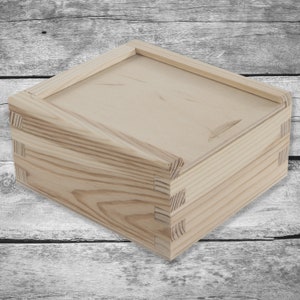 May include: A plain wooden box with a hinged lid. The box is made of light-colored wood with a natural finish. The box is closed and sitting on a wooden surface.