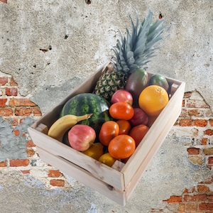 May include: A wooden crate filled with fresh fruit, including a watermelon, pineapple, oranges, apples, and bananas. The crate is sitting on a textured, gray wall.