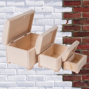 Może przedstawiać: Trzy drewniane pudełka z pokrywkami, włożone jedno w drugie. Pudełka są wykonane z nieoszlifowanego, jasnego drewna i wszystkie są otwarte.