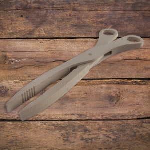 May include: Wooden tongs with a light brown finish. The tongs are made of two pieces of wood that are joined together at the top. The tongs have a serrated grip on one side and a smooth grip on the other side.