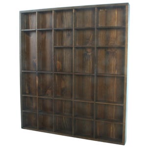 May include: A dark brown wooden display shelf with numerous square compartments. The shelf has a grid-like structure, ideal for organising and showcasing small items. The wood grain is visible, adding a rustic touch. The shelf is made of wood.