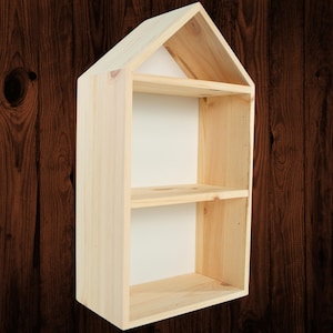 May include: A light-colored wooden shelf in the shape of a house. The shelf has two interior shelves and a pitched roof design. The wood has a natural grain and is unfinished. The interior of the shelf is white.