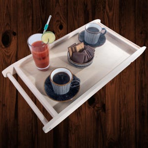 May include: A light wooden serving tray with a glass of red liquid, two cups of coffee, and a small bowl of cookies. The coffee cups and saucers are black with white vertical stripes. A glass of red liquid has a lime slice and a straw.