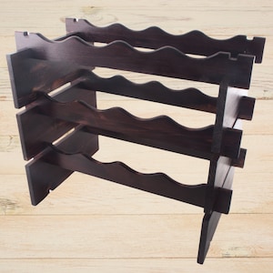 Pode incluir: Um suporte de vinho de madeira castanho escuro com três níveis. Cada nível tem um design ondulado para segurar garrafas de vinho.