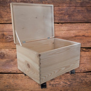 May include: A wooden storage box with a hinged lid and wheels. The box is made of natural wood and has a light brown color. The box is open and empty.