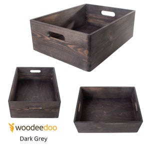 Op de afbeelding: Drie donkergrijze houten opbergdozen met handvatten. De dozen zijn leeg en worden vanuit verschillende hoeken getoond.