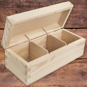 May include: An unfinished wooden box with a hinged lid and three compartments. The box is made of light-colored wood and has a natural wood finish.