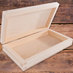 May include: A plain wooden box with a hinged lid, open to reveal the empty interior. The box is made of light-coloured wood and has a natural finish.