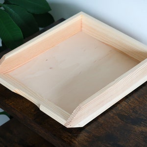 Könnte beinhalten: Ein rechteckiges Tablett aus Naturholz mit leicht abgeschrägter Kante. Das Tablett ist aus unbehandeltem Holz und hat eine glatte Oberfläche.