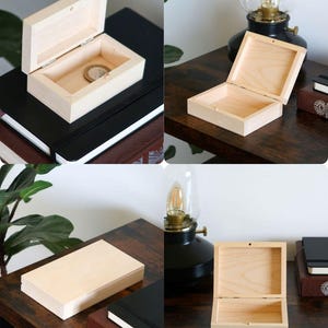 May include: A rectangular light-coloured wooden box with a hinged lid. The box is shown in multiple views, both open and closed, revealing a smooth, unfinished interior surface. One view shows a single metallic coin resting inside the open box.