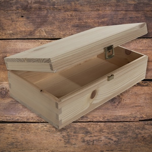 May include: A wooden box with a hinged lid and brass clasps. The box is made of unfinished pine wood and is sitting on a wooden surface.