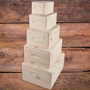 May include: A stack of five wooden boxes with lids, all the same size and shape, arranged in a pyramid shape. The boxes are made of light-coloured wood and have a simple, rustic design.