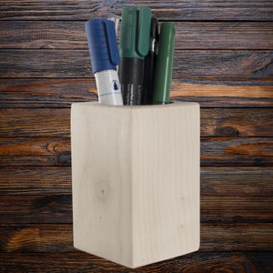 May include: A wooden pencil holder with a light brown finish. Three pens are in the holder, one blue, one green, and one black.