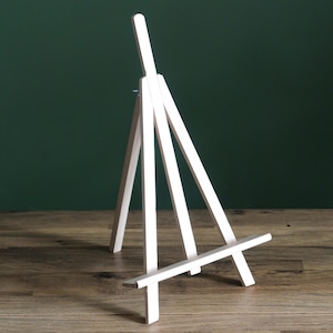 Może przedstawiać: Mały, biały drewniany sztalug, idealny do eksponowania dzieł sztuki lub zdjęć. Sztalug ma trójnożną konstrukcję z odchylanym tyłem dla regulowanego pozycjonowania. Drewno ma gładkie, czyste wykończenie.