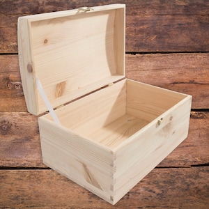 Könnte beinhalten: Eine leere Holzkiste mit einem Scharnierdeckel und Messingverschlüssen. Die Kiste ist aus hellem Holz gefertigt und hat eine natürliche Oberfläche.
