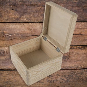 May include: An empty wooden box with a hinged lid. The box is made of light-colored wood and has a natural finish. The lid is open and the box is sitting on a wooden surface.
