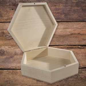 Peut inclure: Une boîte en bois hexagonale ouverte avec un couvercle à charnière. La boîte est en bois clair et a une finition naturelle. La boîte est vide et prête à être remplie de vos objets préférés.